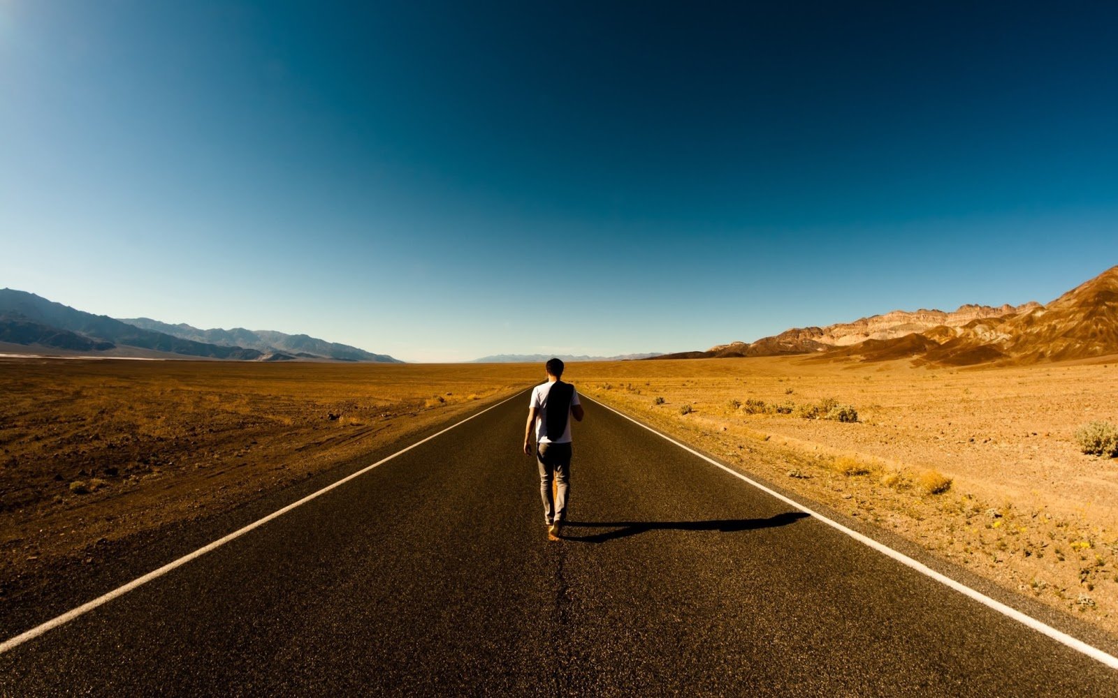 uomo-che-passeggi.jpg uomo che passeggia su una strada in mezzo ad un deserto con montagne